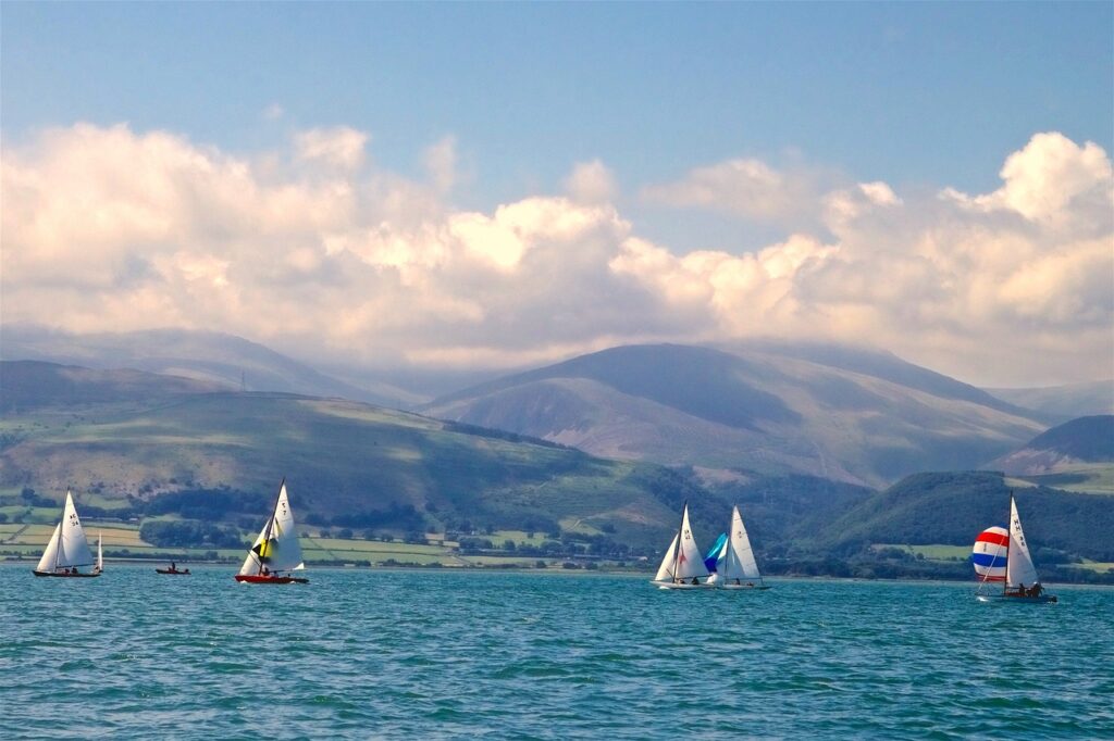 Sali boats with full sails on the water with mountains in the background.