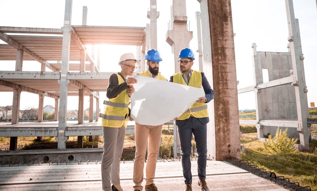 Three men looking at blueprints on a construction site.