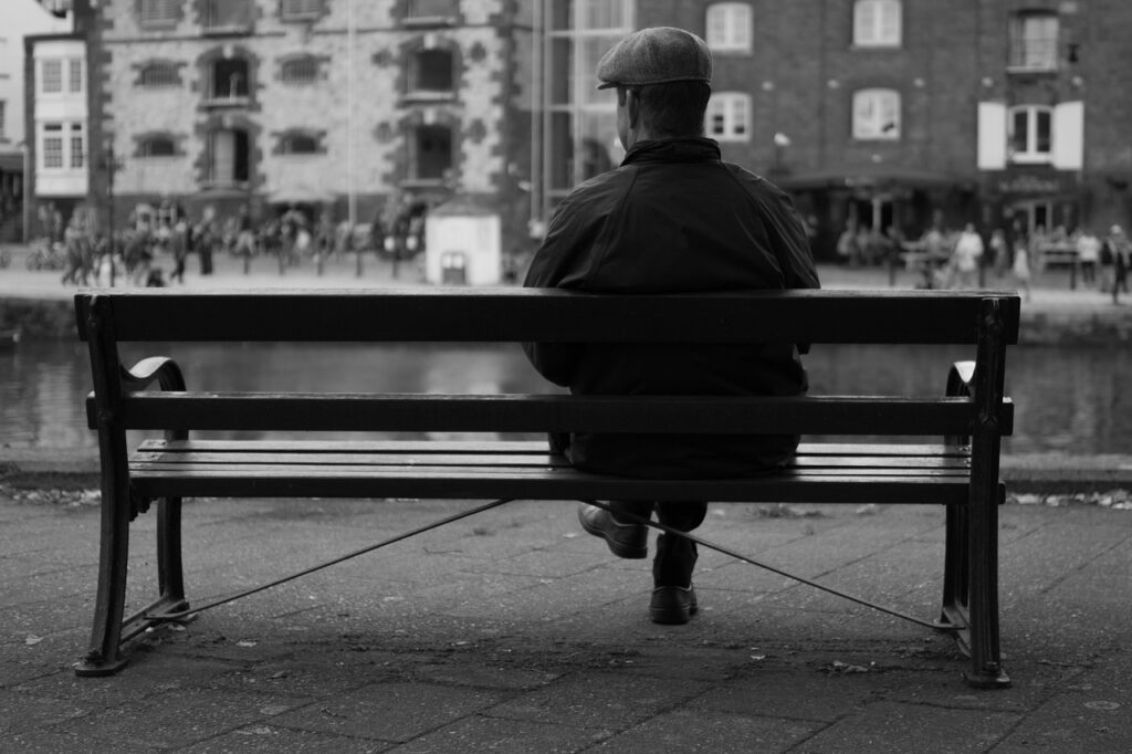 Man sitting on a bench in the city dressed for cool weather.