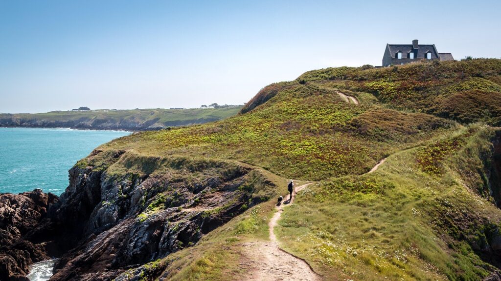 Person walking up a dirt path to a house on a hill overlooking a lake,