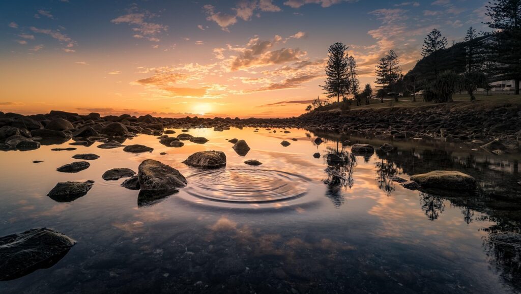 Sunset over a lake bank with a ripple in the water.