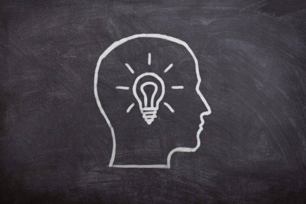 A drawing of a man's head on a chalkboard with a light bulb glowing in the middle.