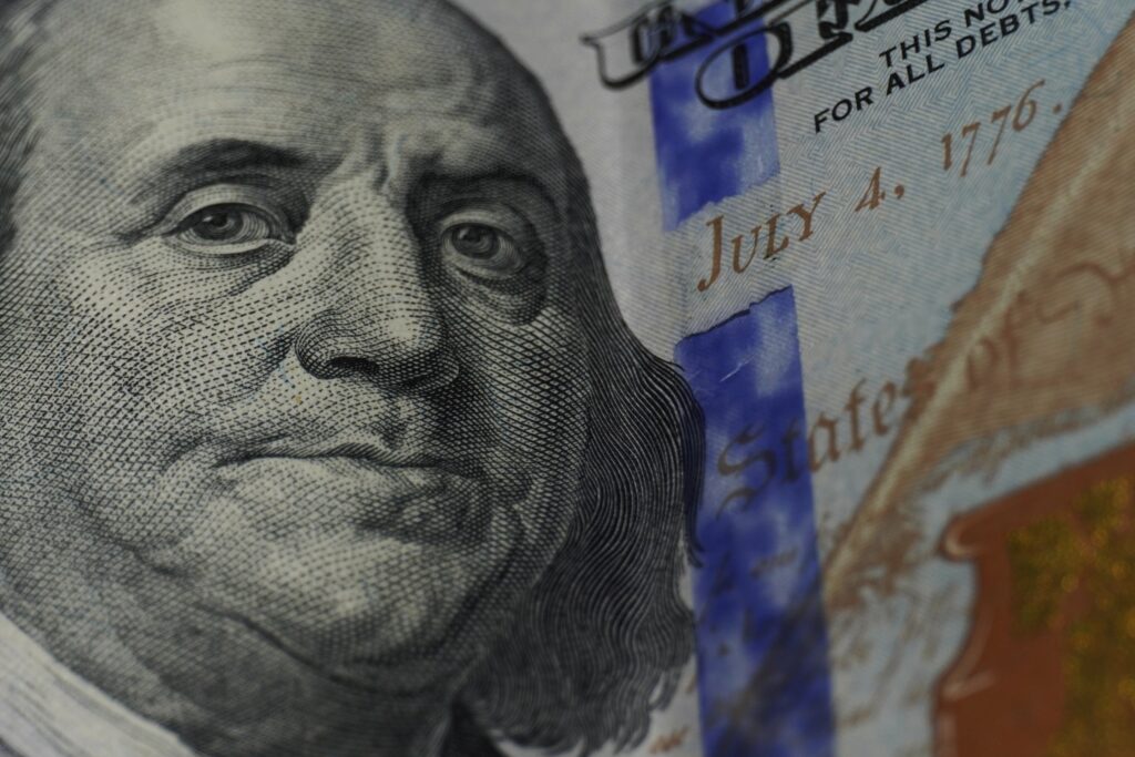 A close up picture of Ben Franklin's face on a $20 bill, with July 4, 1776 in the background.